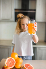 Cute funny little girl drinking freshly squeezed orange juice for healthy breakfast in a white kitchen
