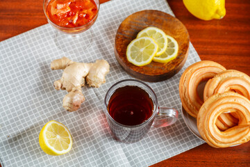 strong tea a cup on the table next to ginger lemon, donuts with cream on a napkin.