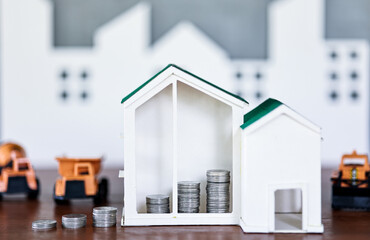 Miniature house models and construction truck models with coin on wooden table. Real estate development or property investment. Construction industry business concept.