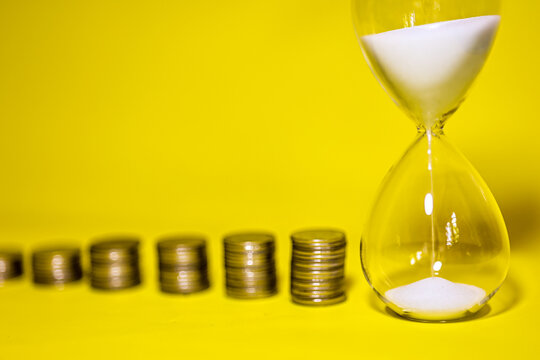 Sand running through the shape of hourglass and coin stack. Countdown timer for business deadline concept.