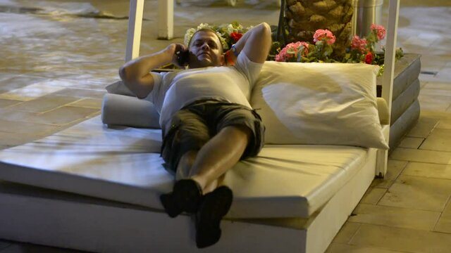 fat man lying on bed near hotel pool and use phone in late evening faint light soft focus