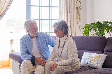 Fototapeta premium Portrait of couple of seniors laughing and having fun together sitting on the sofa of home indoor. Two old and mature people smiling and enjoying joking..