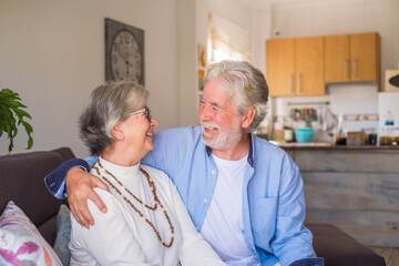 Obraz premium Portrait of couple of seniors laughing and having fun together sitting on the sofa of home indoor. Two old and mature people smiling and enjoying joking..
