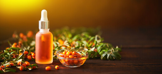 Glass bottle with sea buckthorn oil berries and sea buckthorn branches on wooden background
