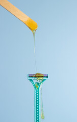 Sugar paste for hair removal against a razor. Sugaring paste drips on a razor on a blue background. The concept of epilation, spa, body care.