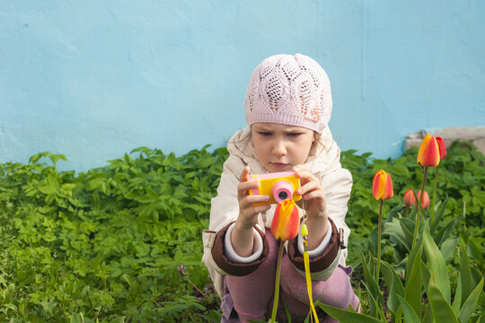 a girl in a white jacket sits with a small camera in front of a tulip