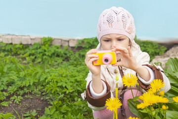 a girl with a yellow children's camera shoots flowers in the garden in the spring