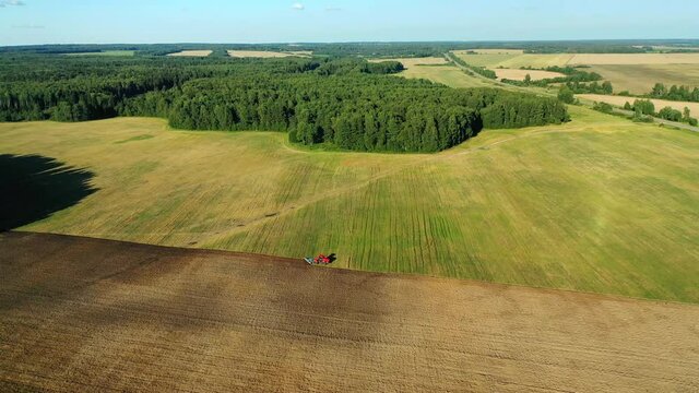 Scenic view of working tractor in the field agricultural field on a summer farm in the evening. Aerial photography, top view drone shot. Agricultural area of Moscow region. Agrarian land 