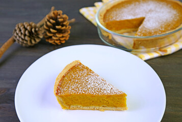 A Slice of Homemade Pumpkin Pie with Blurry Whole Pie for the Concept of Autumn and Thanksgiving