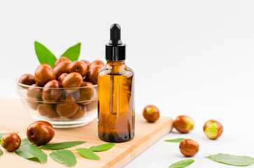 Jojoba oil in a bottle with a dropper on a wooden table with ripe jojoba fruits. Chinese Date Oil and Fruit - obrazy, fototapety, plakaty