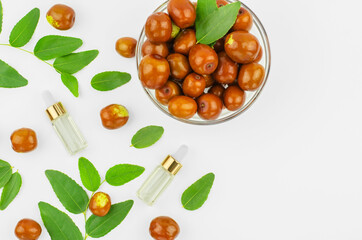 Chinese date oil and fruits, copy space. Jojoba oil in bottles with a dropper on a background with ripe jojoba fruits and green leaves.