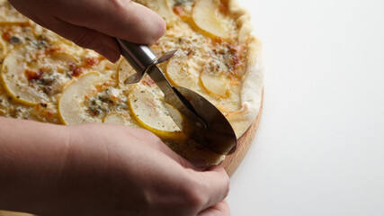 Chef cutting pear fruit pizza with knife on wooden board closeup