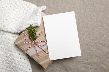Fototapeta na wymiar Christmas greeting card mockup with decorated gift box and knitted sweater on linen background