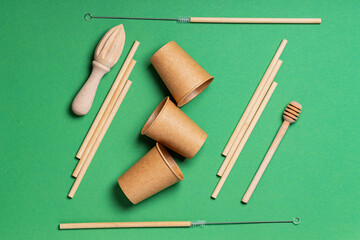 Wooden and paper cutlery on a green background. Wooden cutlery for kitchen and bar with bamboo straws, disposable paper cups and wooden tools. Zero waste. Top view. Flat lay