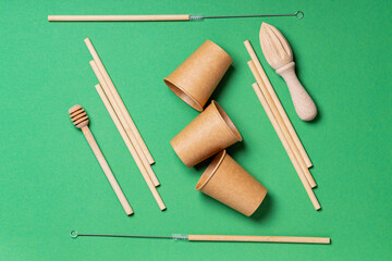 Wooden and paper cutlery on a green background. Wooden cutlery for kitchen and bar with bamboo straws, disposable paper cups and wooden tools. Zero waste. Top view. Flat lay