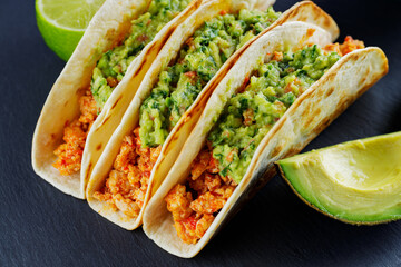 Tacos with chicken and guacamole on a dark background. Mexican tacos with fried minced meat on a slate board. Traditional dish of mexican cuisine