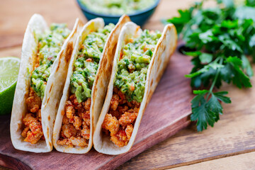 Tacos with fried minced meat and guacamole sauce on a wooden boards. Mexican tacos, cilantro and lime on wooden background. Mexican cuisine. Rustic style