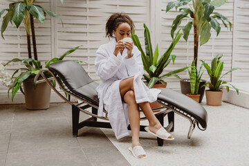 Young African American woman drinking tea and relaxing in spa center.