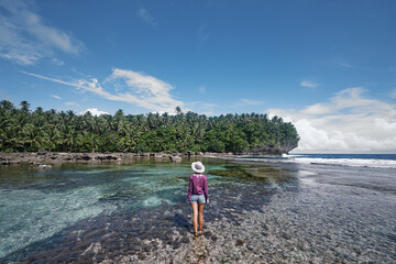 Tropical traveling. Young woman walking by low tide sea reef beach.