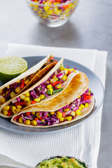 Vegan tacos with corn, purple cabbage and tomatoes on a gray plate. Mexican tacos with vegetables and guacamole on gray background. Close-up