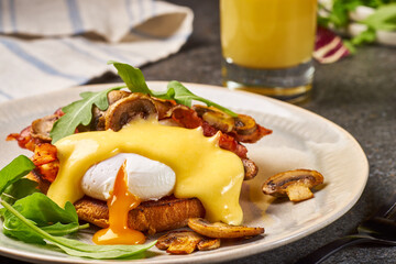 Eggs Benedict with bacon, mushrooms and hollandaise sauce on plate