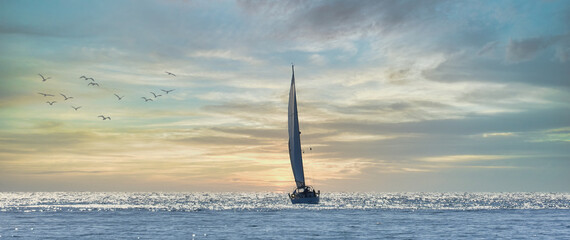 Sailboat sailing towards the horizon at sunset - Powered by Adobe