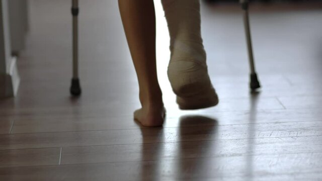 Young woman with crutch and broken leg in cast walking at home, rehabilitation after broken leg accident