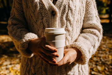 Closeup of a woman wearing a knitted sweater, holding a reusable coffee cup.