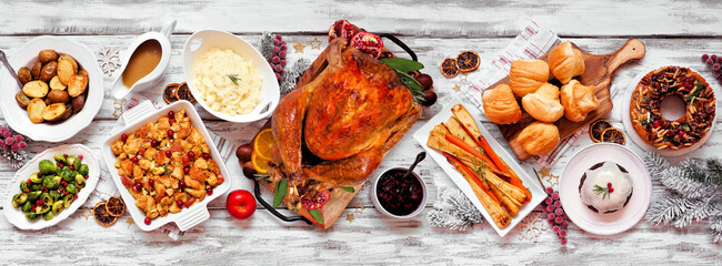 Traditional Christmas turkey dinner. Overhead view table scene on a white wood banner background....