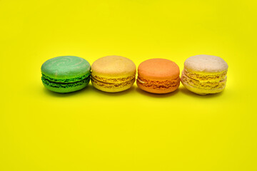 Four different colorful macaron candies lay near each other on yellow background in straight line