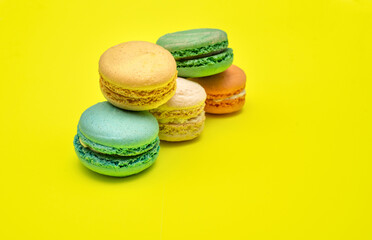 Stack of Five different colorful macaron candies lay on top of each other on yellow background side view