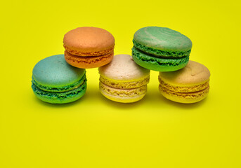 Stack of Five different colorful macaron candies lay on top of each other on yellow background
