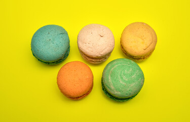 Five different colorful macaron candies lay near each other on yellow background top photo flat lay