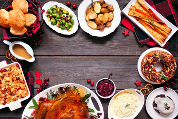 Classic Christmas turkey dinner. Top view frame on a dark wood background. Turkey, potatoes and sides, dressing, fruit cake and plum pudding.