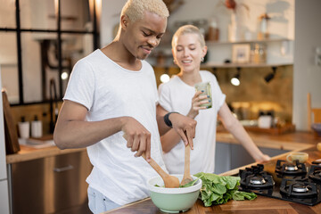 Multiracial couple eating organic salad at home kitchen. Idea of healthy eating. Concept of relationship. Modern domestic lifestyle. Black man and european girl spending time together