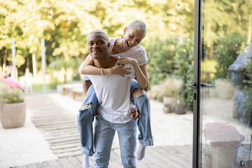 Latin boyfriend giving piggyback ride for his caucasian girlfriend on home terrace. Concept of relationship and enjoying time together. Modern domestic lifestyle. Warm sunny daytime.