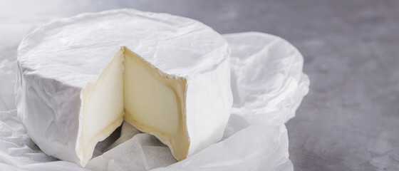 Camembert on a gray cement background. Soft cheese with white mold on parchment paper. Copy space. Top view