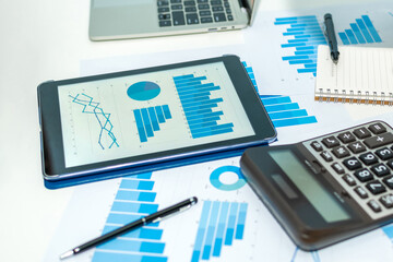 financial graph chart on digital mobile tablet, laptop computer, calculator, business document on workplace desk in meeting room office, business strategy, digital marketing, business meeting concept