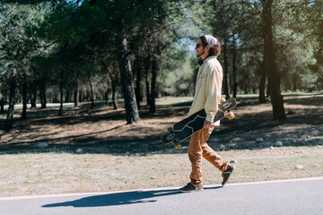 Hipster boy walking down the street with his skateboard in his hand.