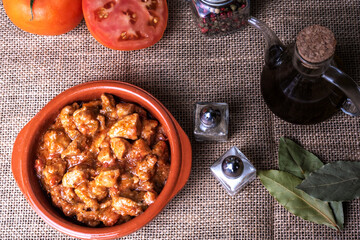 Earthenware plate full of meat with tomato, accompanied by salt, pepper, bay leaf, tomatoes and an...
