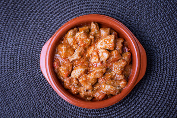 Clay plate filled with meat with tomato and isolated, on a dark tablecloth.