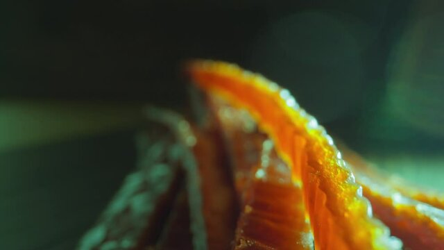 Motion past pile of delicatessen chum salmon stockfish strips lying on dark background at bright lamp light macro close view slow motion