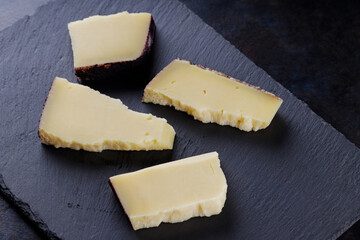Hard cheese pieces on a dark background. Goat cheese on a slate board. Long ripening craft cheese. Copy space
