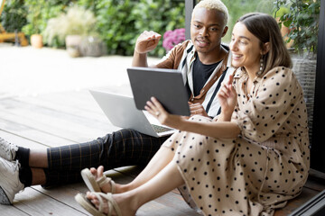 European girl showing something on digital tablet to her focused black boyfriend with laptop....