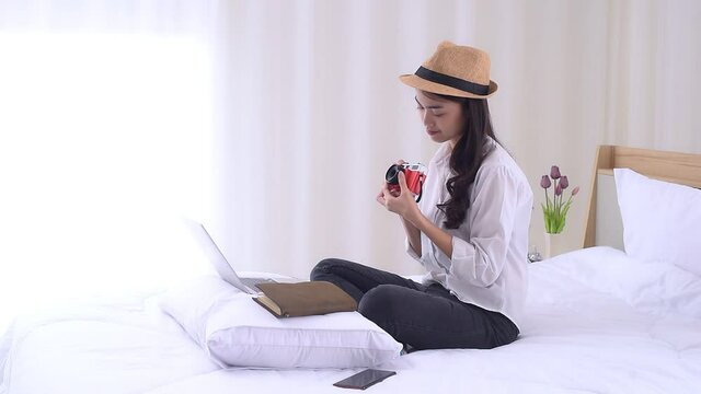 Young Asian woman sitting on the bed and preparing for trip, using a laptop computer to searching information for travel is opening a country after quarantine in hotel during the coronavirus outbreak.