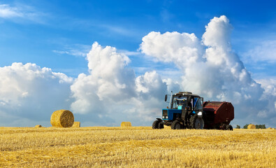 Obraz premium A tractor uses trailed bale machine to collect straw in the field and make round large bales. Agricultural work, baling, baler, hay collection in the summer field.