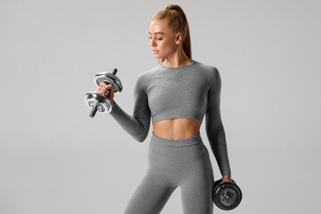 Athletic girl working out with dumbbells on gray background. Fitness woman doing exercise
