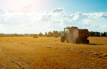 Obraz premium tractor uses trailed bale machine to collect straw in the field and make round large bales. Agricultural work, baling, baler, hay collection in the summer field.