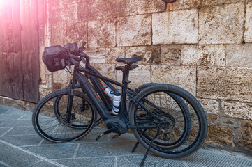 Fototapeta na wymiar San Quirico d'Orcia, Tuscany, Italy. August 2020. Two ebikes parked on the pavement, one has a flat front wheel.