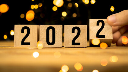 Hand changes wooden cubes to 2022 Happy New Year concept background with bokeh